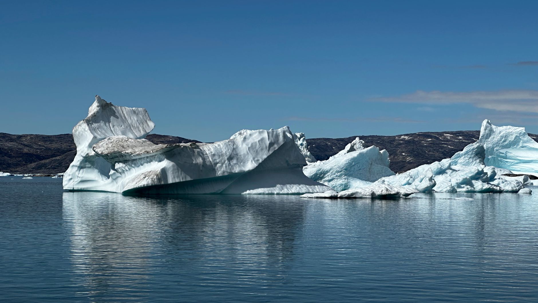 Snow-covered Greenland mountains rising above a calm fjord used by summer ferries