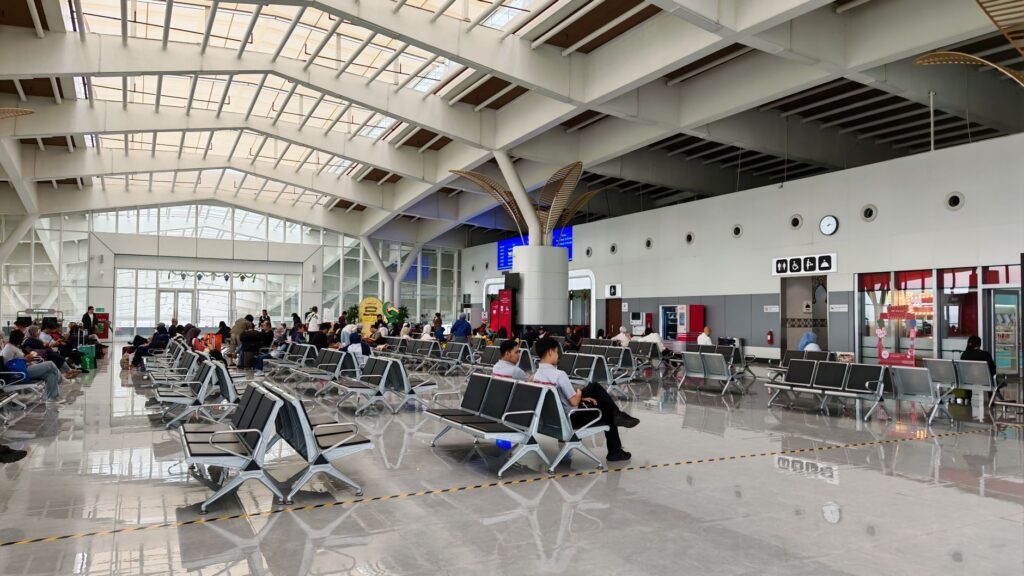 Passengers waiting in a modern airport transit lounge with seats and large windows between connecting flights